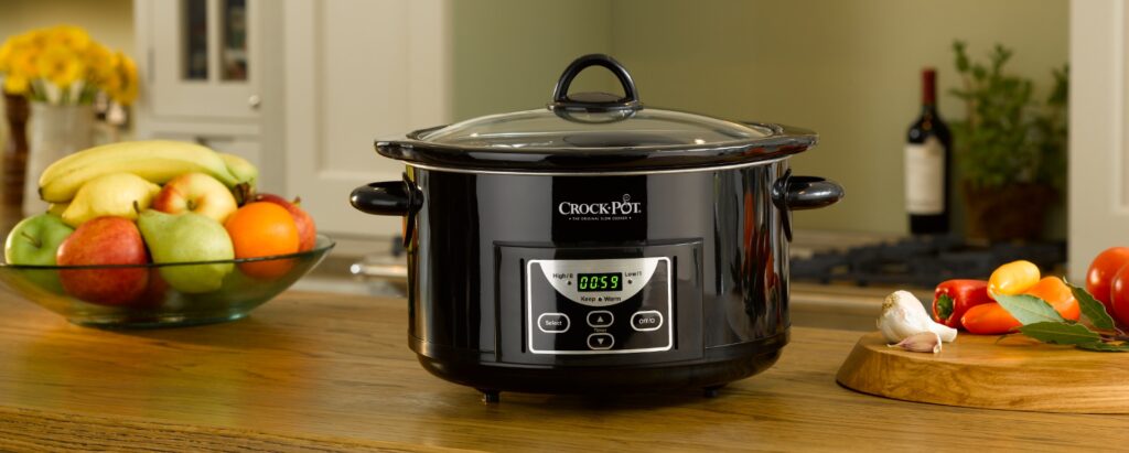 Slow cooker på köksbänk med färska frukter och grönsaker.