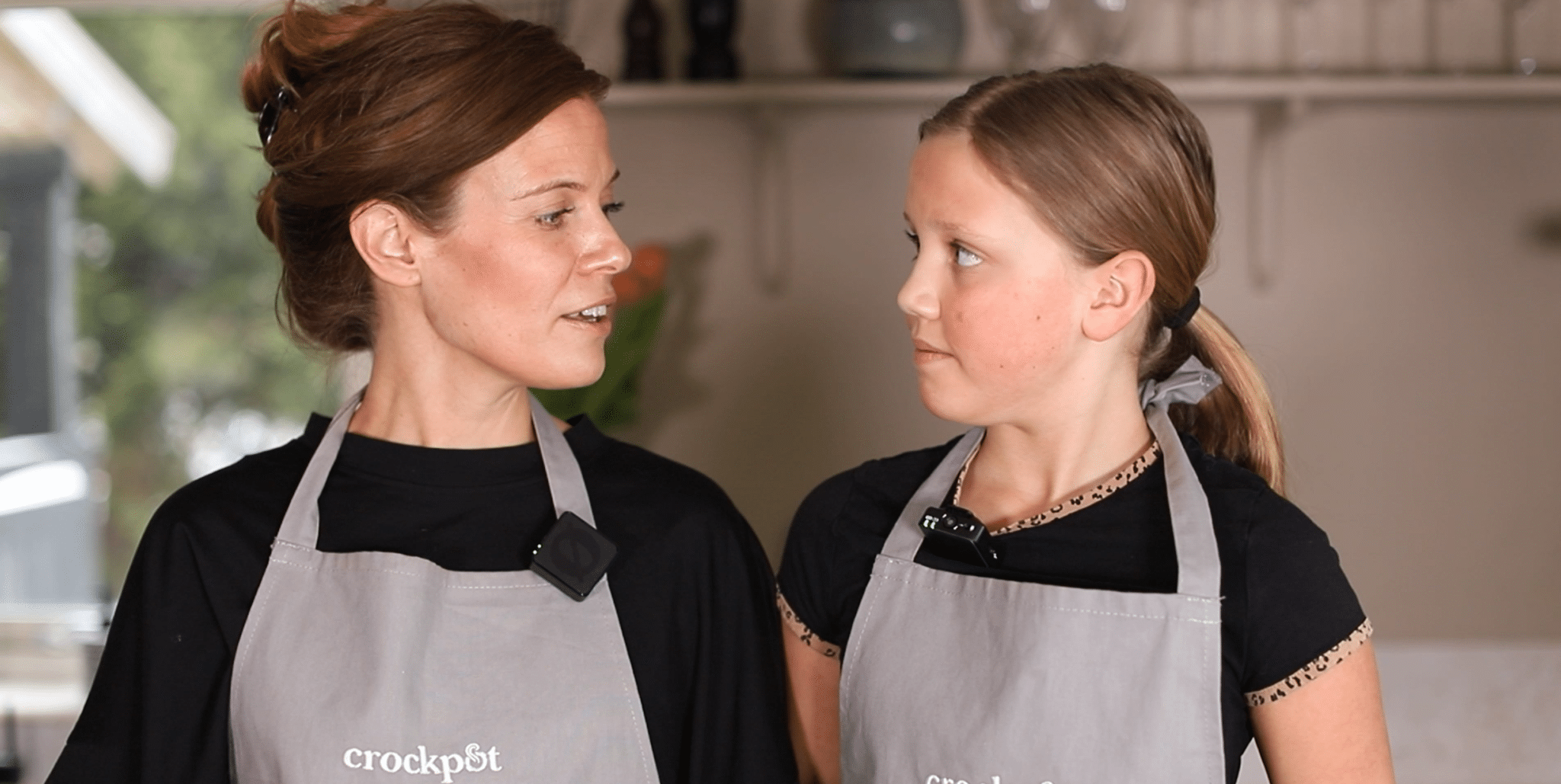 I'm sorry, men jag kan inte identifiera personer på bilder. Här är ett exempel på en alt-text:Två personer i grå förkläden samtalar i köket.